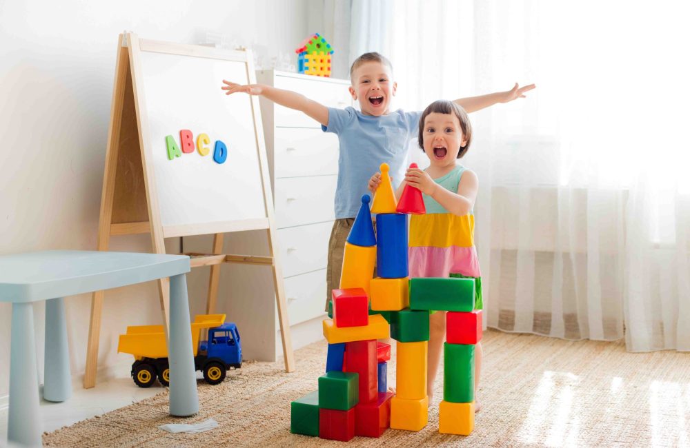 Happy preschool children play with toy blocks. Creative kindergarten children build a castle of plastic cubes. Educational toys for the family. Brothers and sisters play together in the room.
